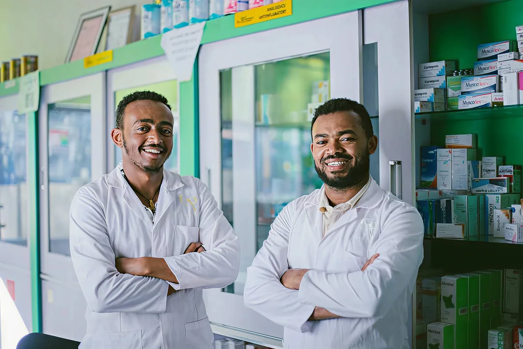 Two pharmacists in white lab coats standing with arms crossed inside a pharmacy, representing Pharmalink’s innovative healthcare approach